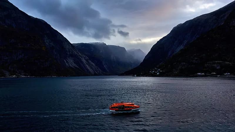 An orange launch crossing a fjord at dusk